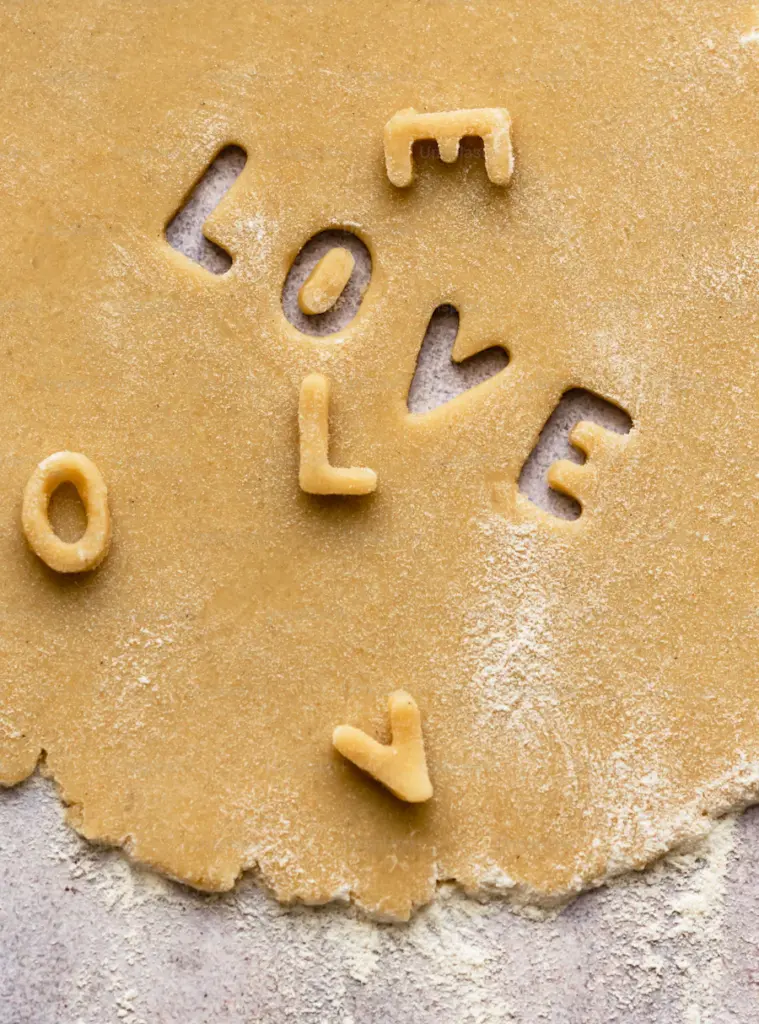 The inspirational word "LOVE" cut out in letters from a piece of dough that is rolled out on a concrete counter top.