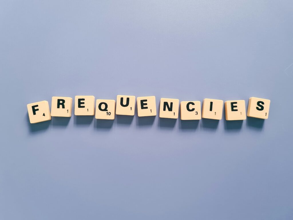The word "frequencies" spelled out in scrabble tiles against a blue background