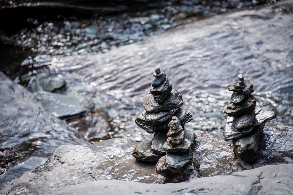 Three tall rock stacks placed along a river creating frequencies beneficial for meditation