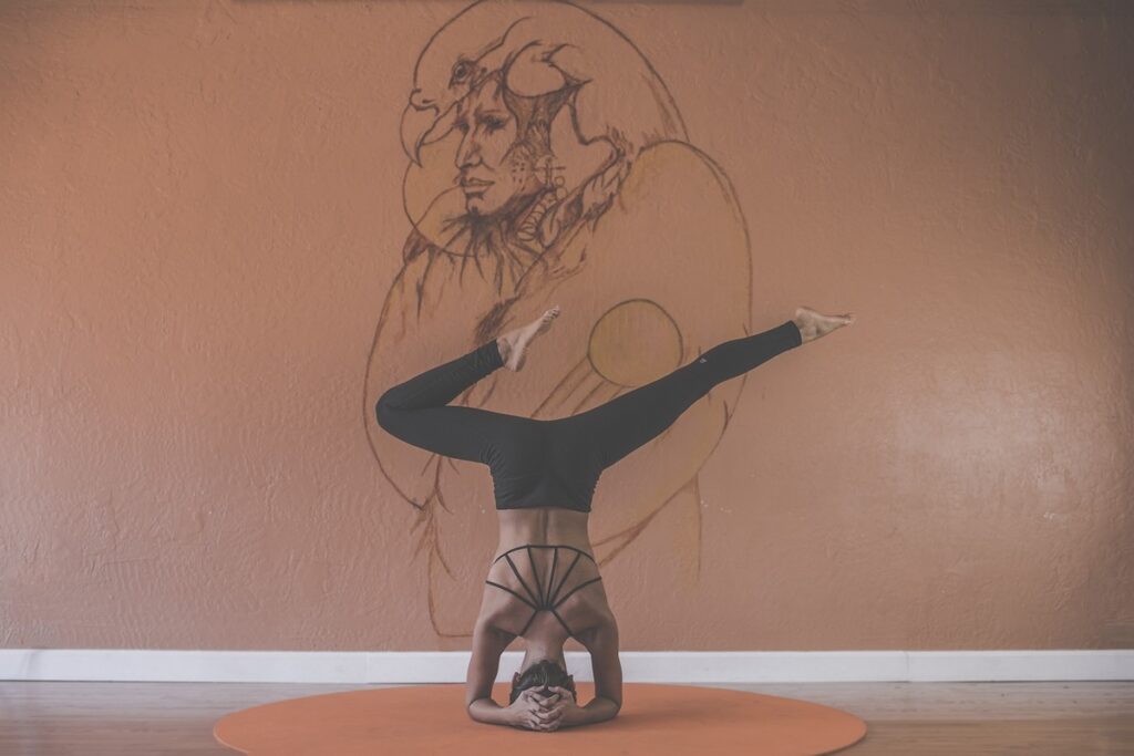 Woman practicing yoga and meditation in headstand on an orange circular rug in front of a sketch image of a native person with an eagle headdress