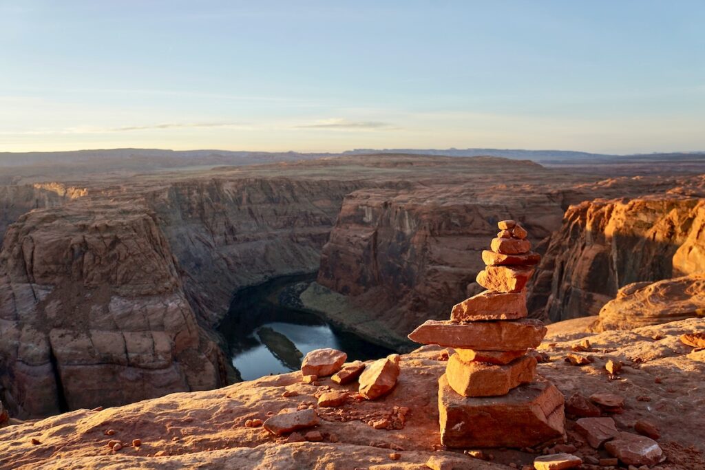 Tall rock cairn in front of an image of a river in a desert canyon called horseshoe bend