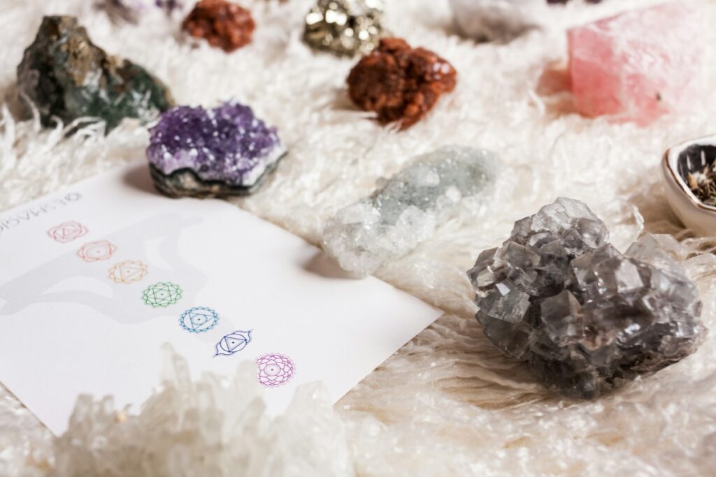 An array of colorful stones, laid out on a sheepskin, next to a sheet of paper displaying colorful chakra symbols.